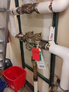 A wall-mounted backflow preventer assembly with brass valves and an inspection tag.