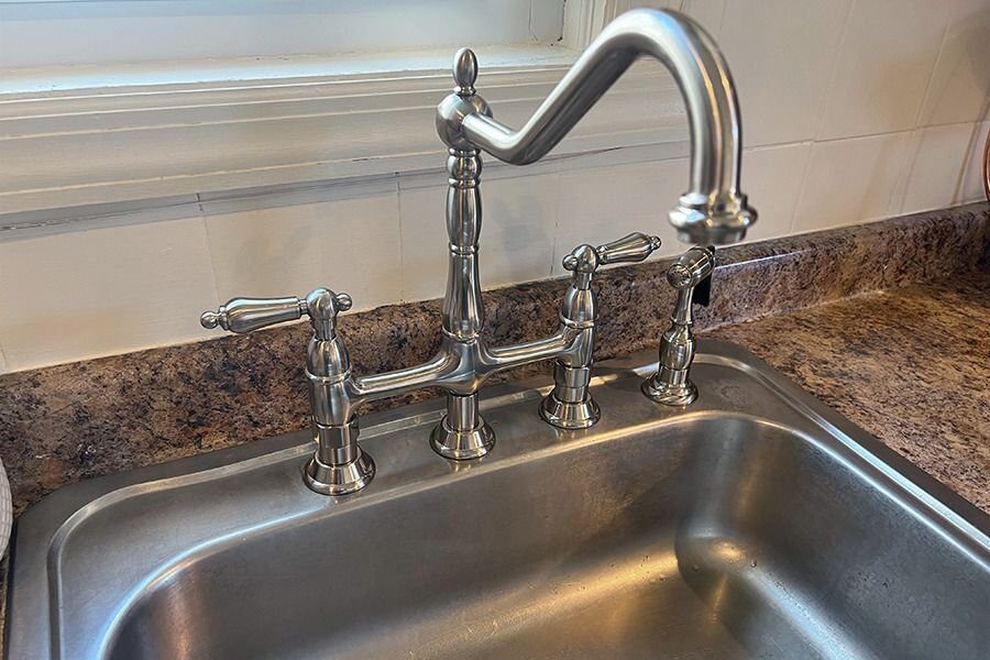 A newly installed chrome bridge faucet above a stainless steel sink set in a granite countertop.