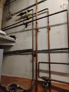 Copper and black iron supply piping running along a mechanical room wall.