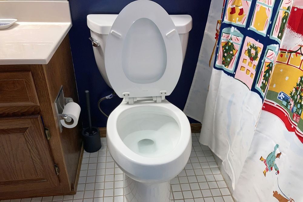 A newly installed white toilet in a residential bathroom with tile flooring and a wood vanity.